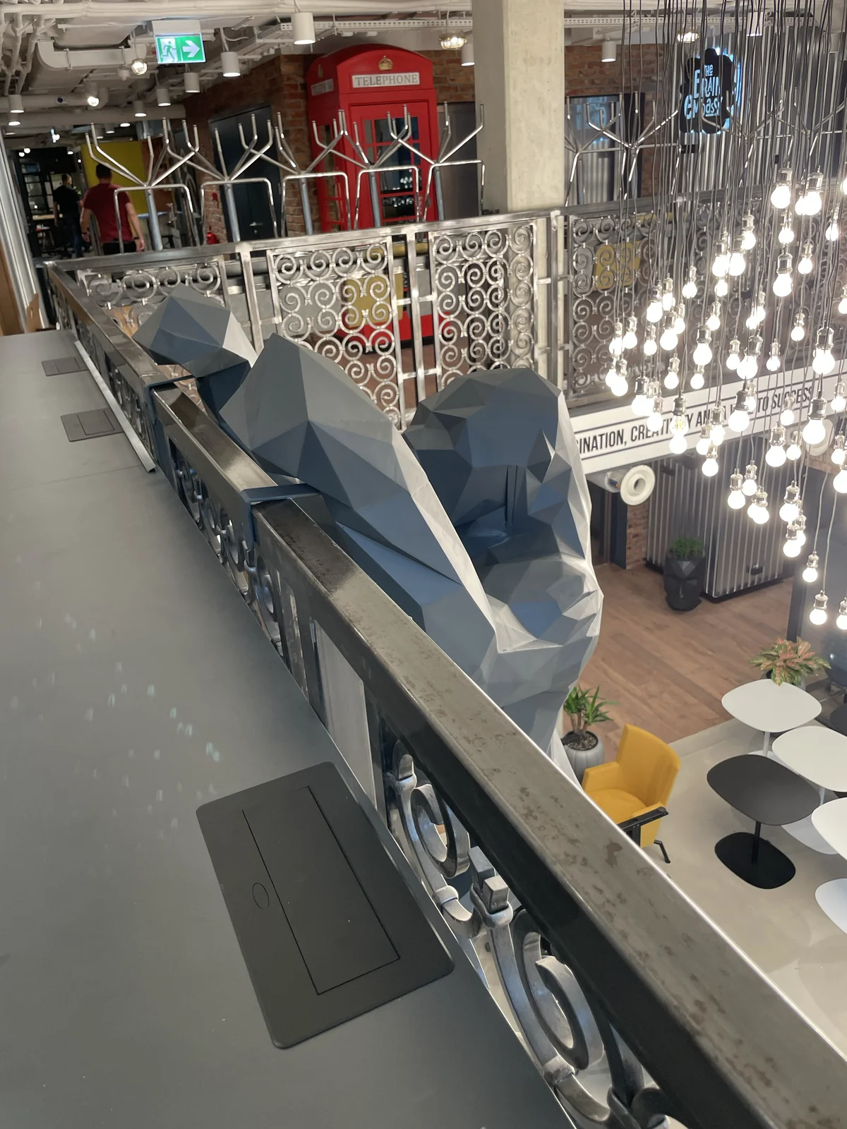 Szara geometryczna instalacja przy balustradzie we wnętrzu z wiszącymi lampami