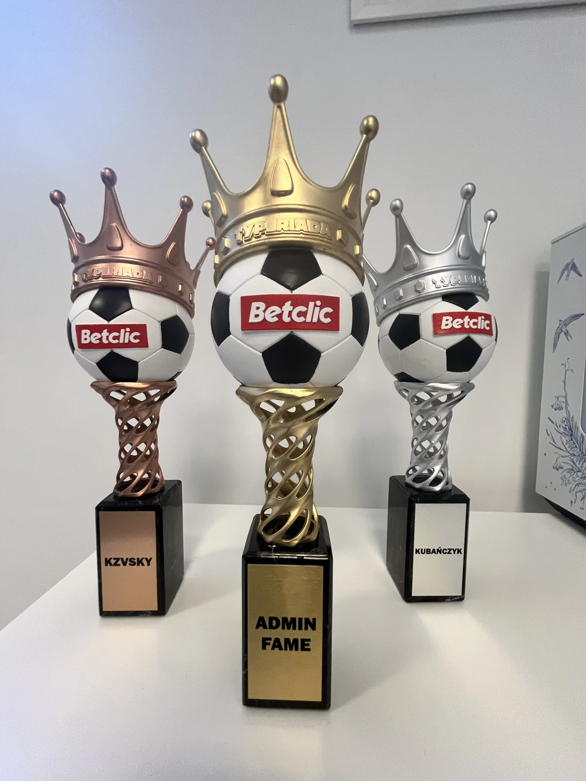 Trzy wykończone trofea z piłkami i koronami w kolorze złota, srebra i miedzi