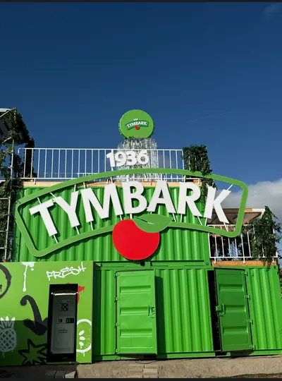 Zielona konstrukcja ekspozycyjna z napisem Tymbark i przestrzennym jabłkiem