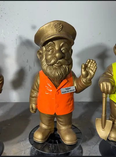 Złota figurka krasnala w pomarańczowym stroju roboczym, z łopatą