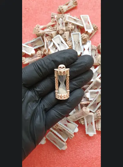 Miniaturowa klepsydra ozdobiona czaszkami w dłoni w czarnej rękawiczce